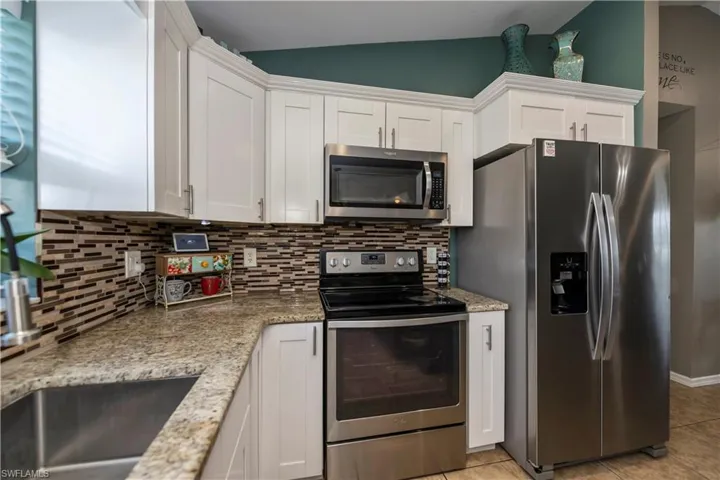 Kitchen featuring decorative backsplash, vaulted ceiling, white cabinetry, and stainless steel appliances