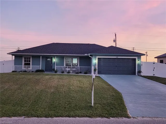 Ranch-style house with covered porch, a garage, and a lawn