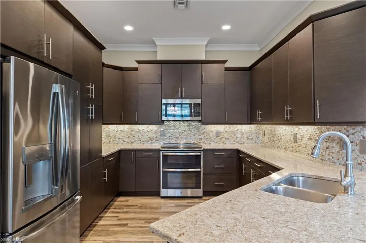 Kitchen featuring stainless steel appliances, ornamental molding, sink, decorative backsplash, and dark brown cabinetry