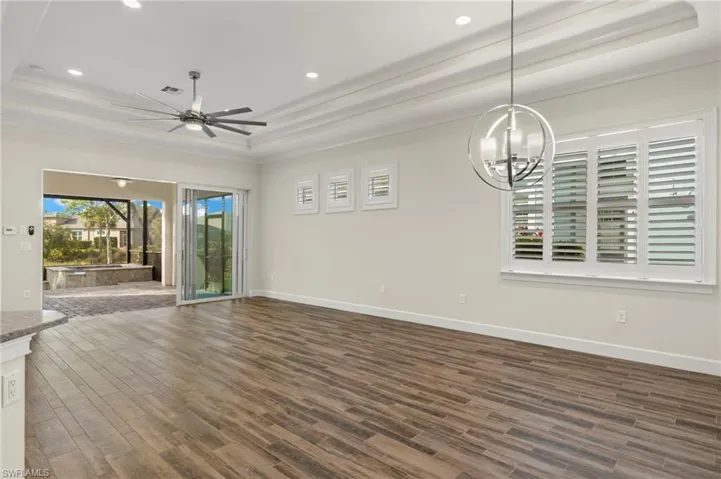 Family room with views to covered lanai, pool & spa & lake views. Ceiling fan with notable chandelier, ornamental molding, dark wood-type flooring, and a tray ceiling