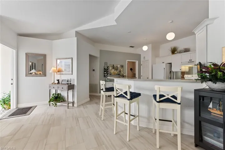 Kitchen with a breakfast bar, stainless steel refrigerator, decorative light fixtures, white cabinets, and kitchen peninsula