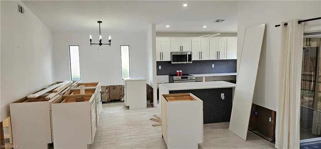 Kitchen featuring pendant lighting, appliances with stainless steel finishes, tasteful backsplash, white cabinets, and a kitchen island
