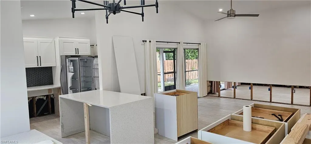 Kitchen with a kitchen island, stainless steel refrigerator, high vaulted ceiling, white cabinets, and light hardwood / wood-style flooring