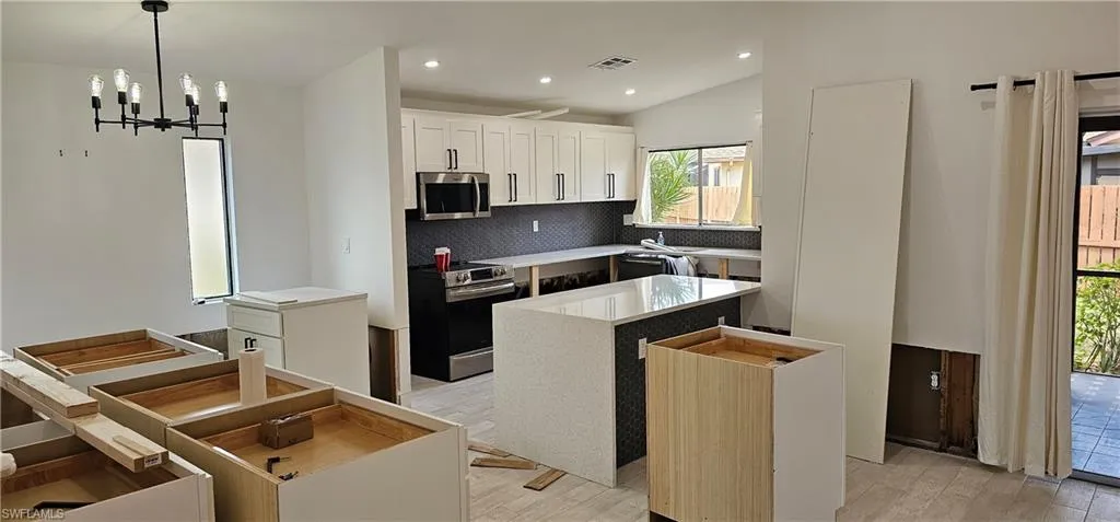 Kitchen featuring tasteful backsplash, a center island, appliances with stainless steel finishes, pendant lighting, and white cabinets