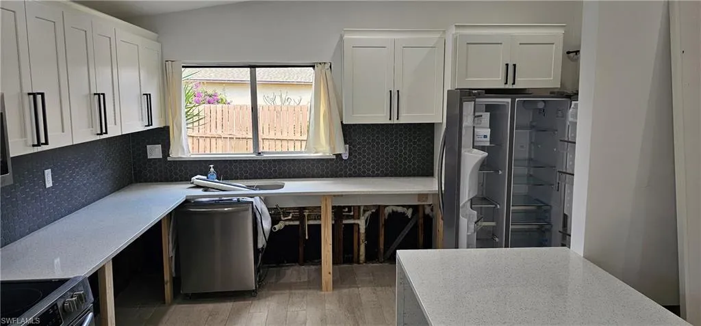 Kitchen with white cabinetry, appliances with stainless steel finishes, wood-type flooring, and backsplash