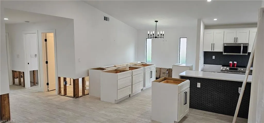 Kitchen featuring pendant lighting, light hardwood / wood-style flooring, stainless steel appliances, a notable chandelier, and white cabinets
