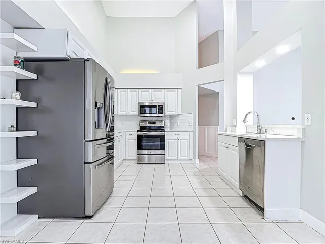 Kitchen featuring open shelves, a high ceiling, light countertops, a sink, and stainless steel appliances