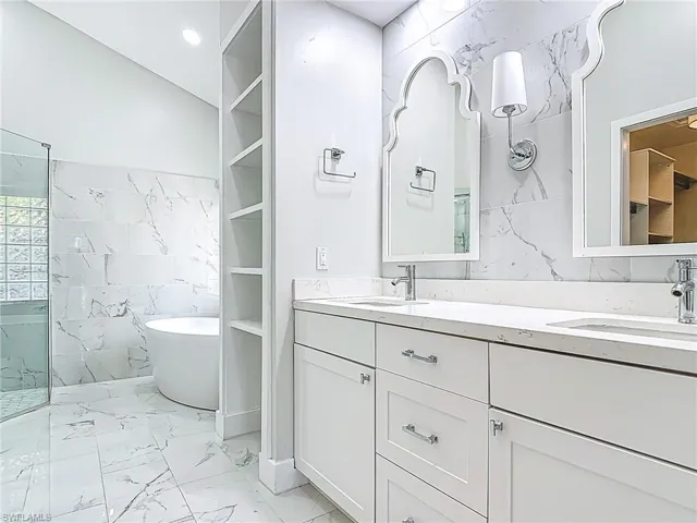 Bathroom featuring a sink, marble finish floor, a soaking tub, and tile walls