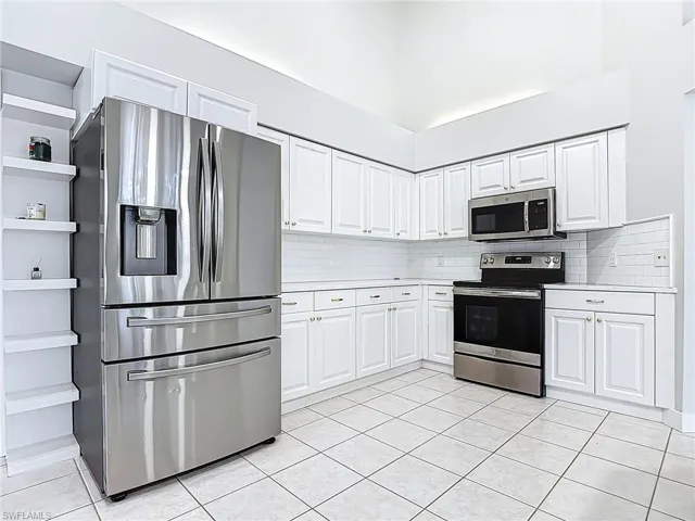 Kitchen featuring light countertops, backsplash, appliances with stainless steel finishes, and light tile patterned floors