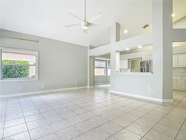 Unfurnished living room featuring ceiling fan, visible vents, light tile patterned floors, high vaulted ceiling, and baseboards