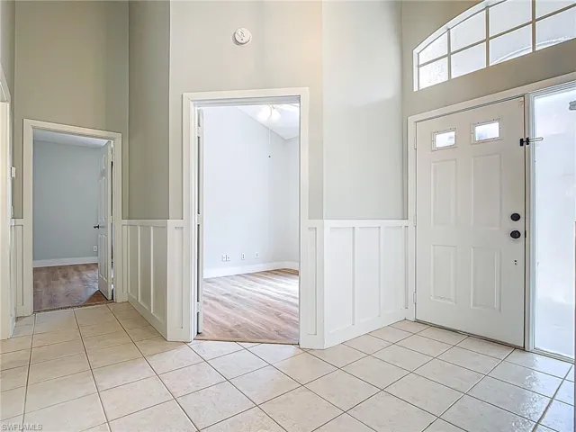 Entryway featuring a decorative wall, a high ceiling, wainscoting, and light tile patterned flooring