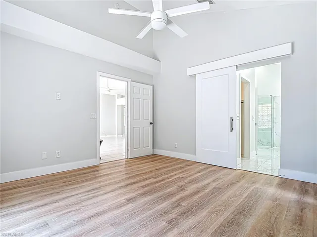 Unfurnished bedroom with baseboards, light wood finished floors, ensuite bathroom, and high vaulted ceiling