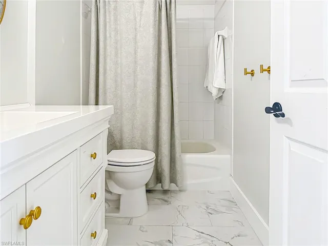 Full bath with shower / bath combo, vanity, toilet, marble finish floor, and baseboards