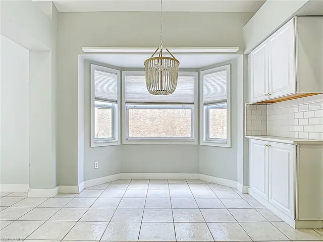 Unfurnished dining area featuring light tile patterned flooring, baseboards, and an inviting chandelier
