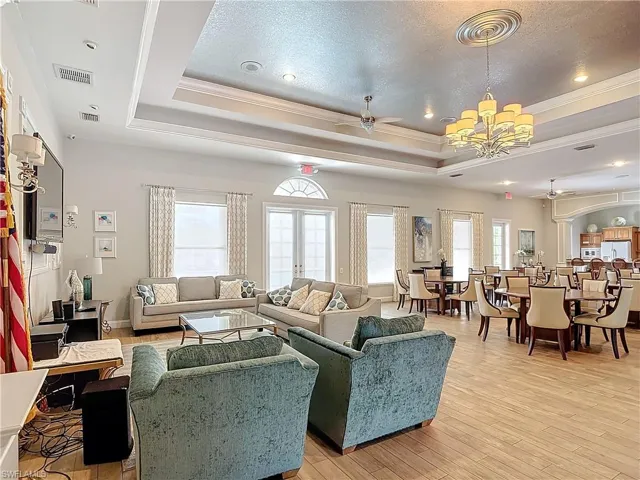 Living room featuring light hardwood / wood-style floors, ceiling fan with notable chandelier, a tray ceiling, ornamental molding, and a textured ceiling
