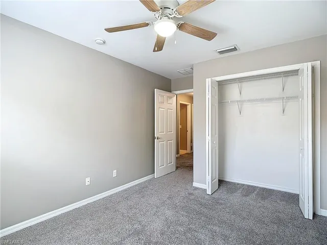 Unfurnished bedroom featuring dark carpet, a closet, and ceiling fan