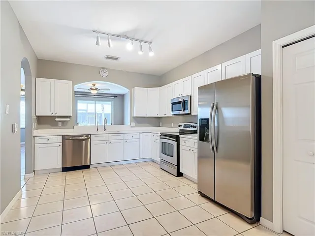 Kitchen with track lighting, appliances with stainless steel finishes, white cabinetry, and light tile floors