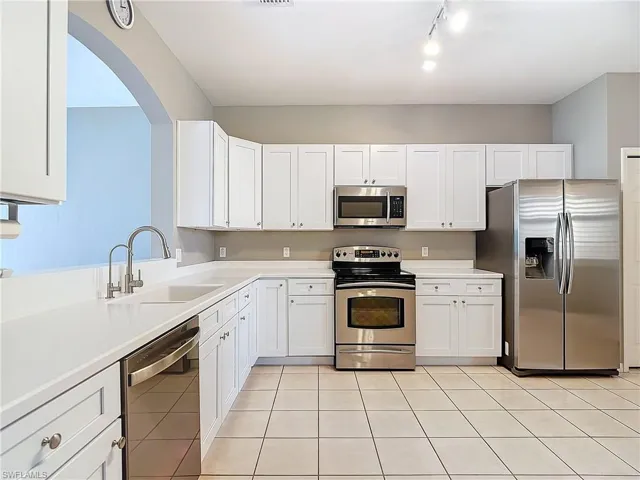 Kitchen featuring white cabinetry, appliances with stainless steel finishes, sink, track lighting, and light tile flooring