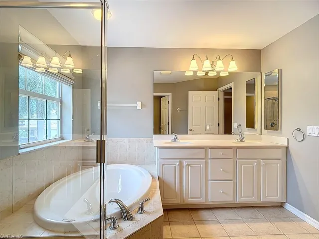 Bathroom with tile floors, large vanity, tiled bath, and double sink