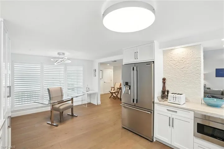 Kitchen with stainless steel appliances, white cabinetry, light wood-style flooring, and light stone counters