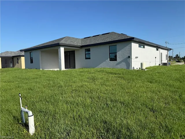 Rear view of property with stucco siding, a yard, and a shingled roof
