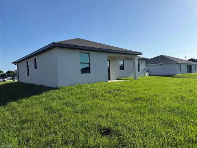 Back of property featuring stucco siding, a yard, and roof with shingles