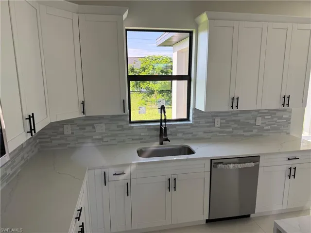 Kitchen featuring white cabinetry, dishwasher, light stone countertops, and backsplash