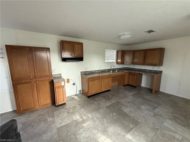 Kitchen with brown cabinets, a textured ceiling, a sink, and dark countertops