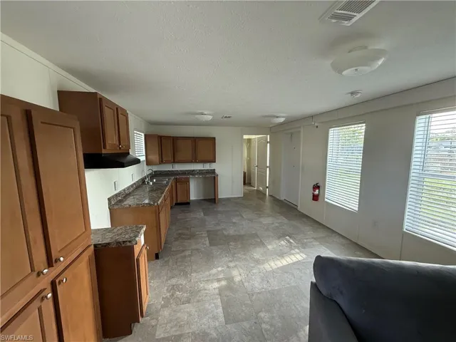 Kitchen featuring brown cabinetry, dark countertops, a sink, a textured ceiling, and stone finish flooring