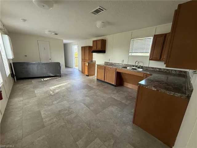Kitchen featuring a sink, healthy amount of natural light, brown cabinets, dark countertops, and a textured ceiling