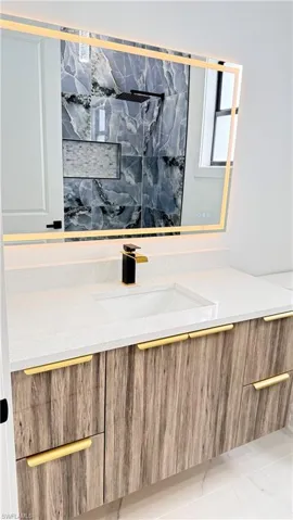 Floating wood-finish vanity with gold-tone hardware, white countertop, integrated rectangular sink, and two-tone faucet