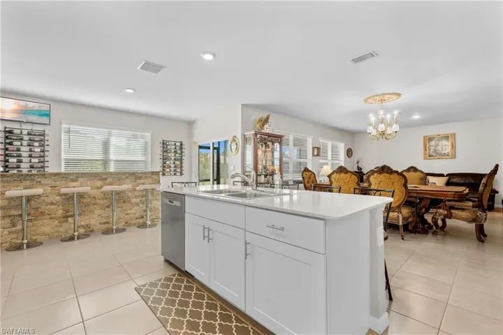 Kitchen featuring white cabinets, a center island with sink, dishwasher, suspended lighting, and light tile patterned flooring