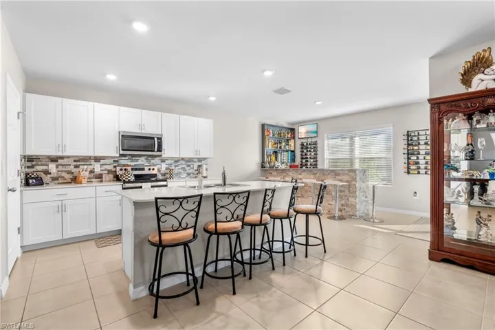 Kitchen with a breakfast bar, stainless steel appliances, a center island with sink, white cabinetry, and light tile patterned floors