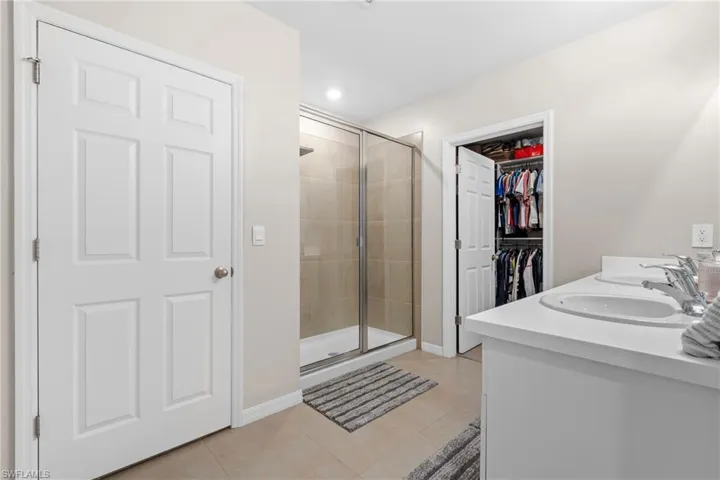 Full bathroom with a stall shower, double vanity, light tile patterned floors, and a spacious closet