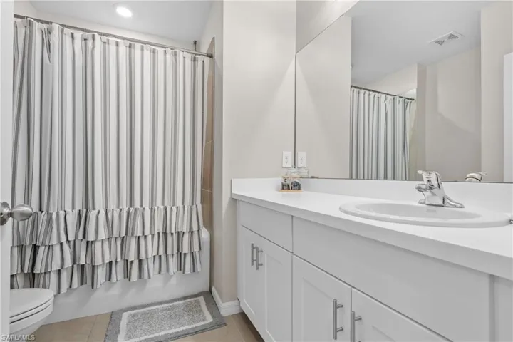 Bathroom with vanity, shower / bathtub combination with curtain, and light tile patterned floors