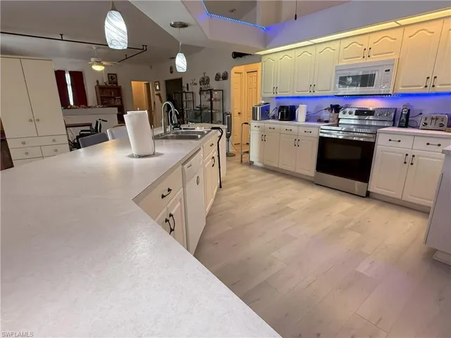 Kitchen with white appliances, ceiling fan, sink, light hardwood / wood-style floors, and hanging light fixtures