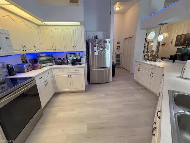 Kitchen featuring a towering ceiling, light wood-type flooring, stainless steel appliances, sink, and decorative light fixtures