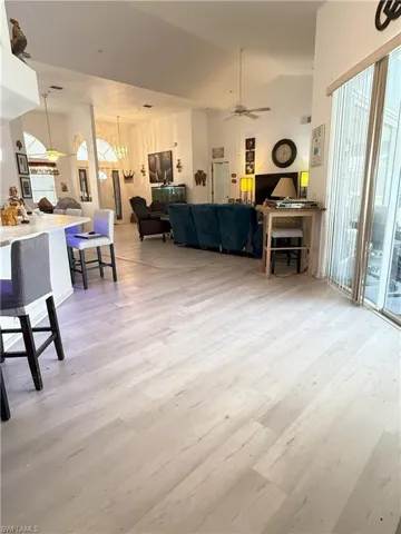 Living room featuring vaulted ceiling, wood-type flooring, and ceiling fan with notable chandelier