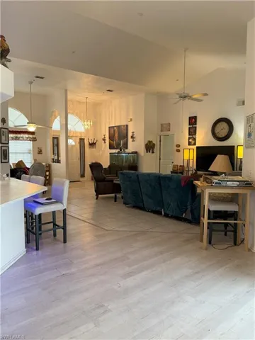 Living room with ceiling fan with notable chandelier, light hardwood / wood-style floors, and lofted ceiling