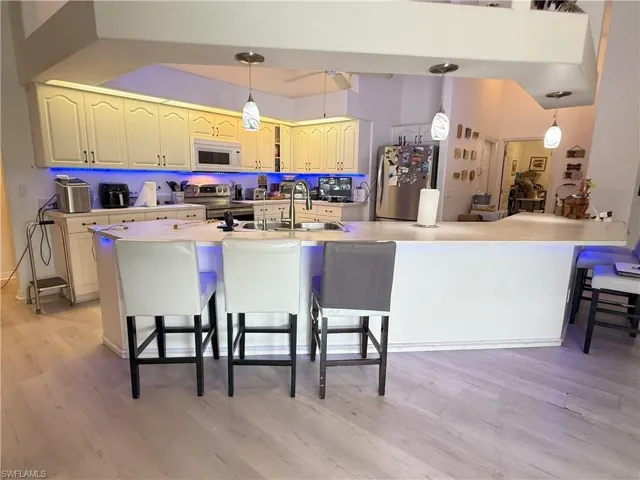 Kitchen with a kitchen breakfast bar, light wood-type flooring, stainless steel appliances, and hanging light fixtures
