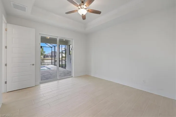 Empty room featuring a tray ceiling, a sunroom, wood tiled floors, a ceiling fan, and crown molding