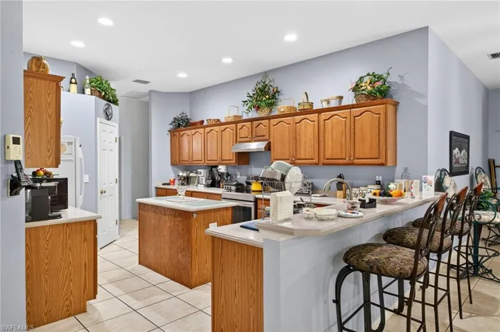Kitchen with wood finish cabinetry, a peninsula, a kitchen island, light tile patterned floors, and light countertops