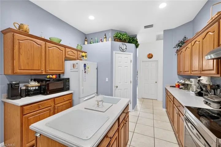 Kitchen with a center island, freestanding refrigerator, black microwave, light countertops, and wood finish cabinets