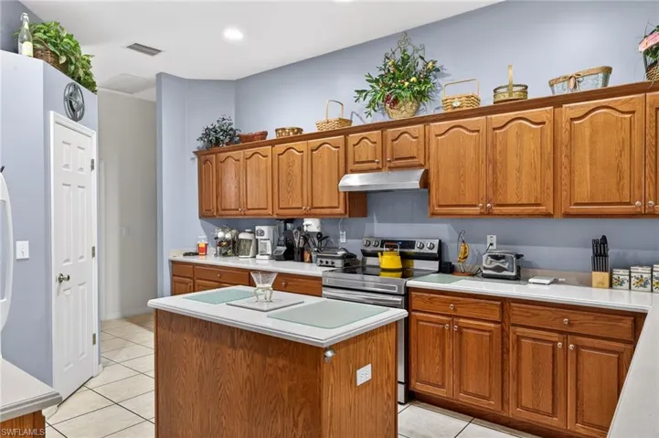 Kitchen featuring wood finish cabinetry, light tile patterned flooring, a kitchen island, stainless steel range with electric cooktop, and recessed lighting