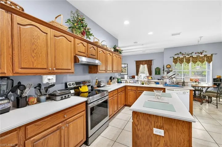 Kitchen with stainless steel electric range oven, a peninsula, wood finish cabinets, light countertops, and light tile patterned floors