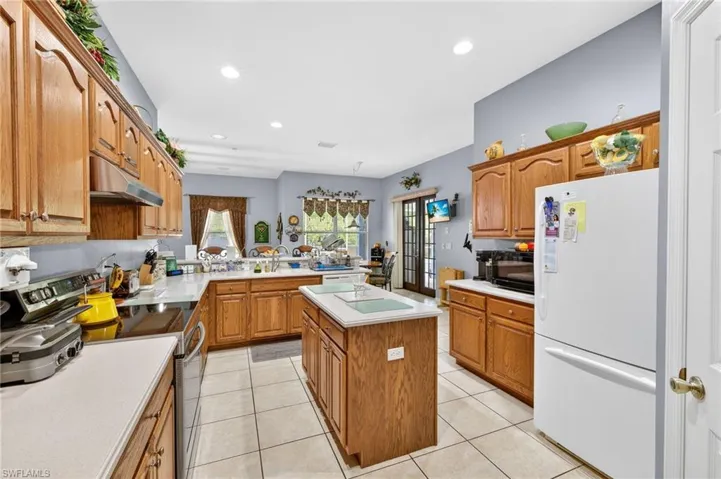 Kitchen with electric range, freestanding refrigerator, wood finish cabinets, light countertops, and recessed lighting