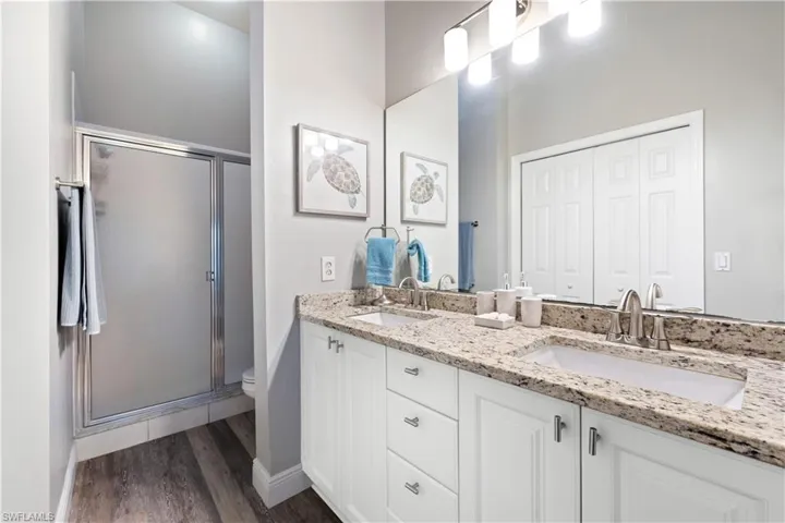 Bathroom with double vanity, a stall shower, and wood finished floors