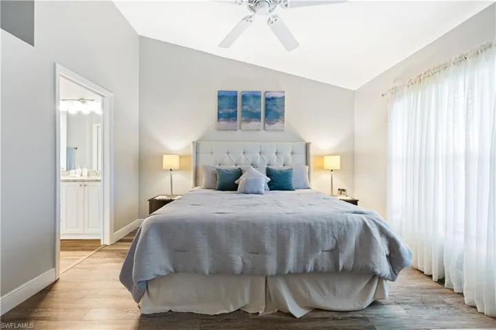 Bedroom featuring vaulted ceiling, light wood-style floors, ensuite bath, and a ceiling fan