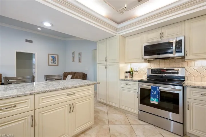 Kitchen with light stone countertops, ornamental molding, stainless steel appliances, cream cabinets, and tasteful backsplash