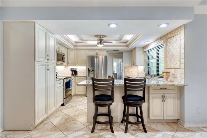 Kitchen featuring stainless steel appliances, light stone counters, a breakfast bar area, and a tray ceiling